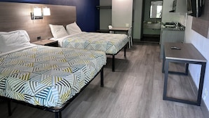 Ein Hotelzimmer mit zwei Betten, einem kleinen Tisch, einem Schreibtisch, einem Spiegel und einer Küchenzeile.