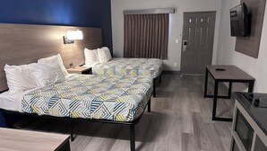 Ein Hotelzimmer mit zwei Betten, einem Schreibtisch, einem an der Wand befestigten Fernseher und einer Tür.