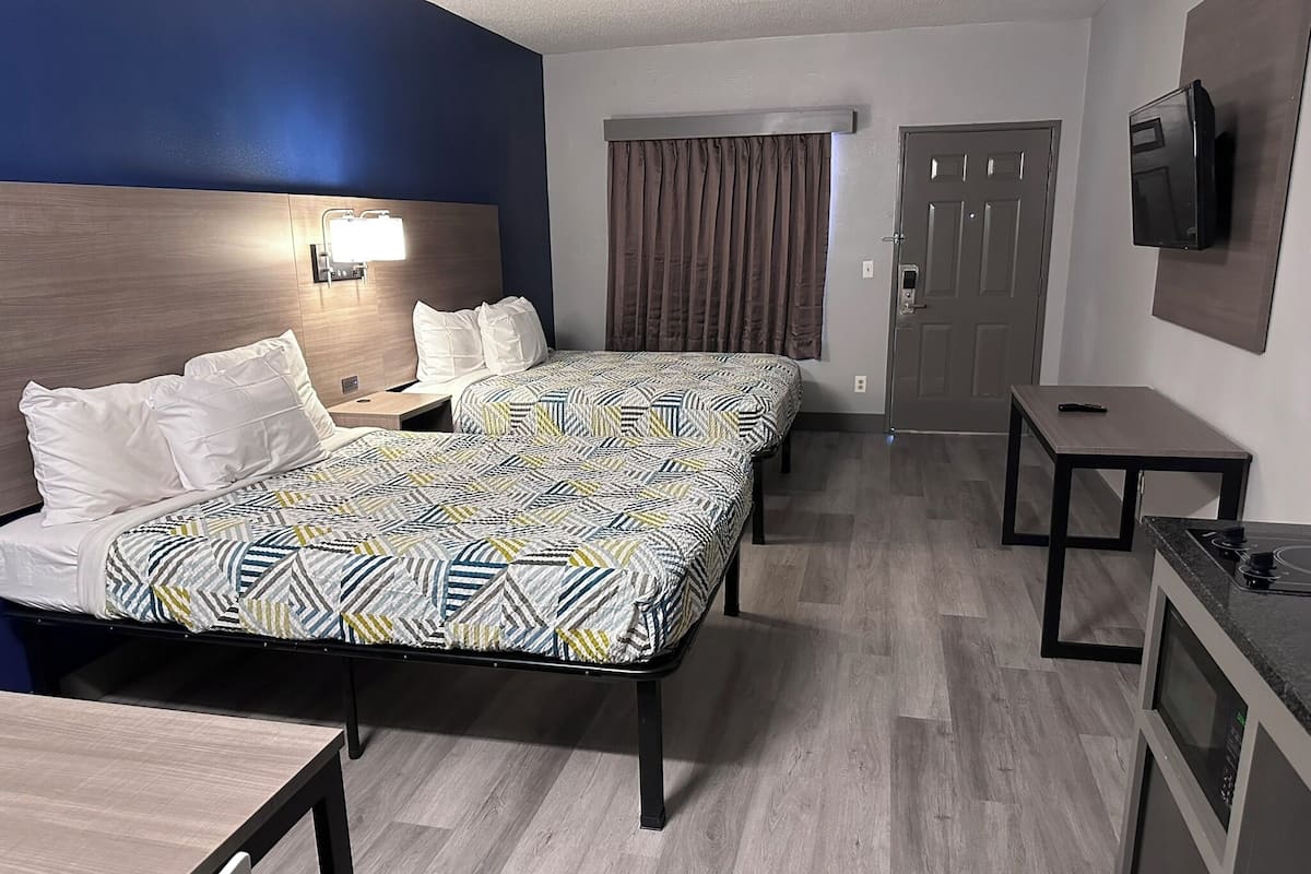 A hotel room with two beds, a desk, a TV mounted on the wall, and a door.