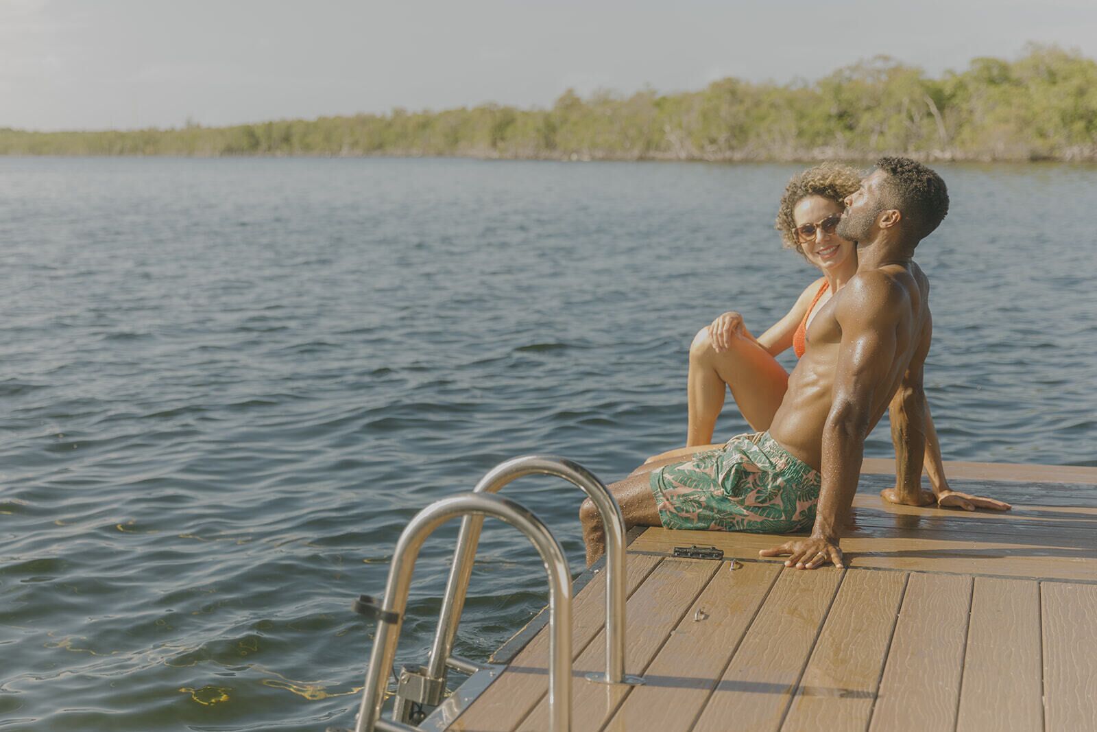 A wooden deck extending over a body of water, with a metal ladder leading into the water.