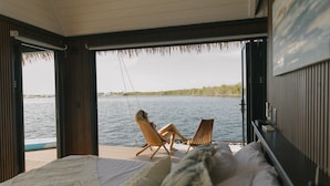 A room with a bed, two chairs, and a view of a lake. - Premium Floating Bungalow by Stay Ombi (Key Largo)