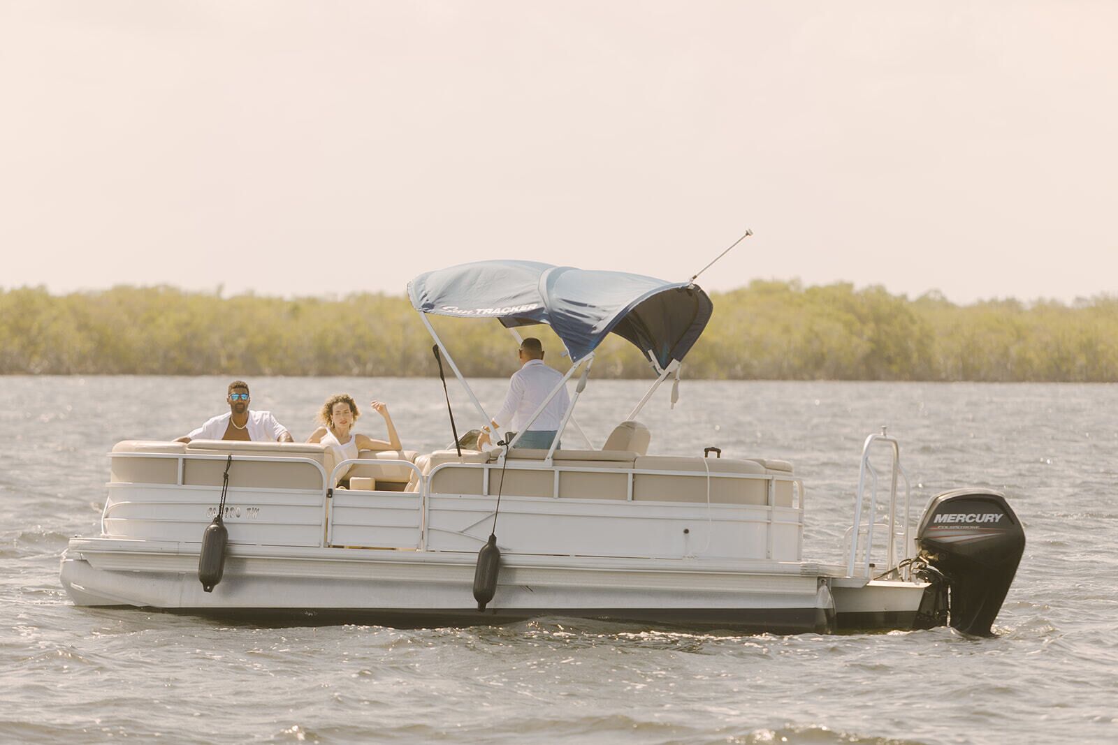 A pontoon boat with a canopy, a Mercury outboard motor, and passengers.