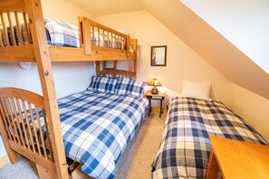 A dormitory room with bunk beds, a bedside table with a lamp, and a framed picture on the wall.