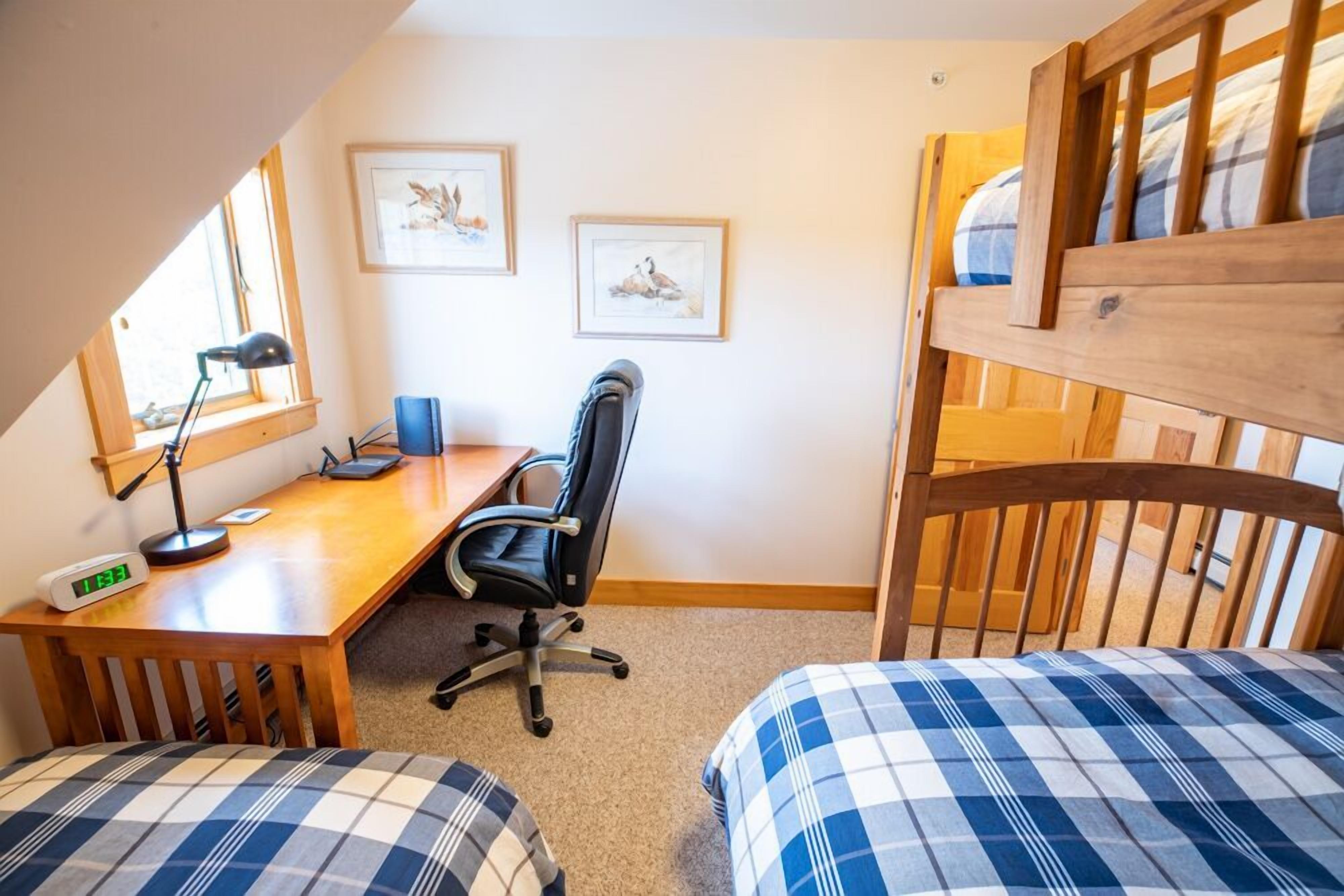 A bedroom with a bunk bed, a desk with a chair, a computer, and two framed pictures on the wall.