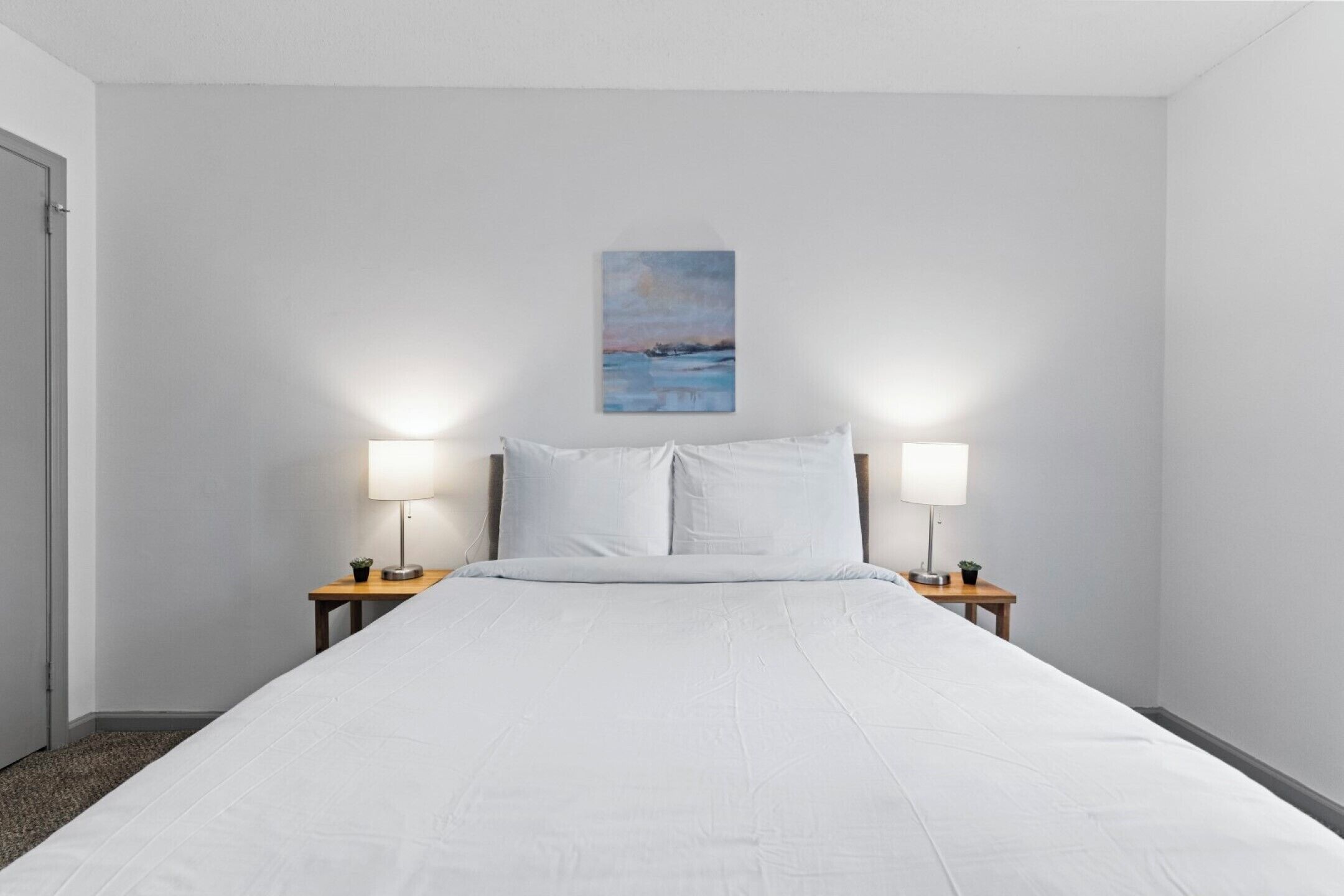 Habitación de hotel con una cama grande, dos lámparas de noche, una mesita de noche con lámpara y un cuadro en la pared.