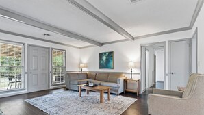 Ein geräumiges Wohnzimmer mit einem großen Sofa, einem Couchtisch und einem gemusterten Teppich. Auf Nachttischen stehen zwei Lampen, und an der Wand hängt ein Gemälde.