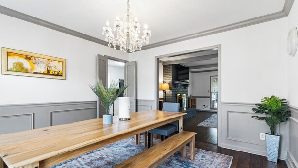 Ein Essbereich mit Holztisch, Bänken, einer Pendelleuchte, einem Blumentopf und einem gemusterten Teppich.