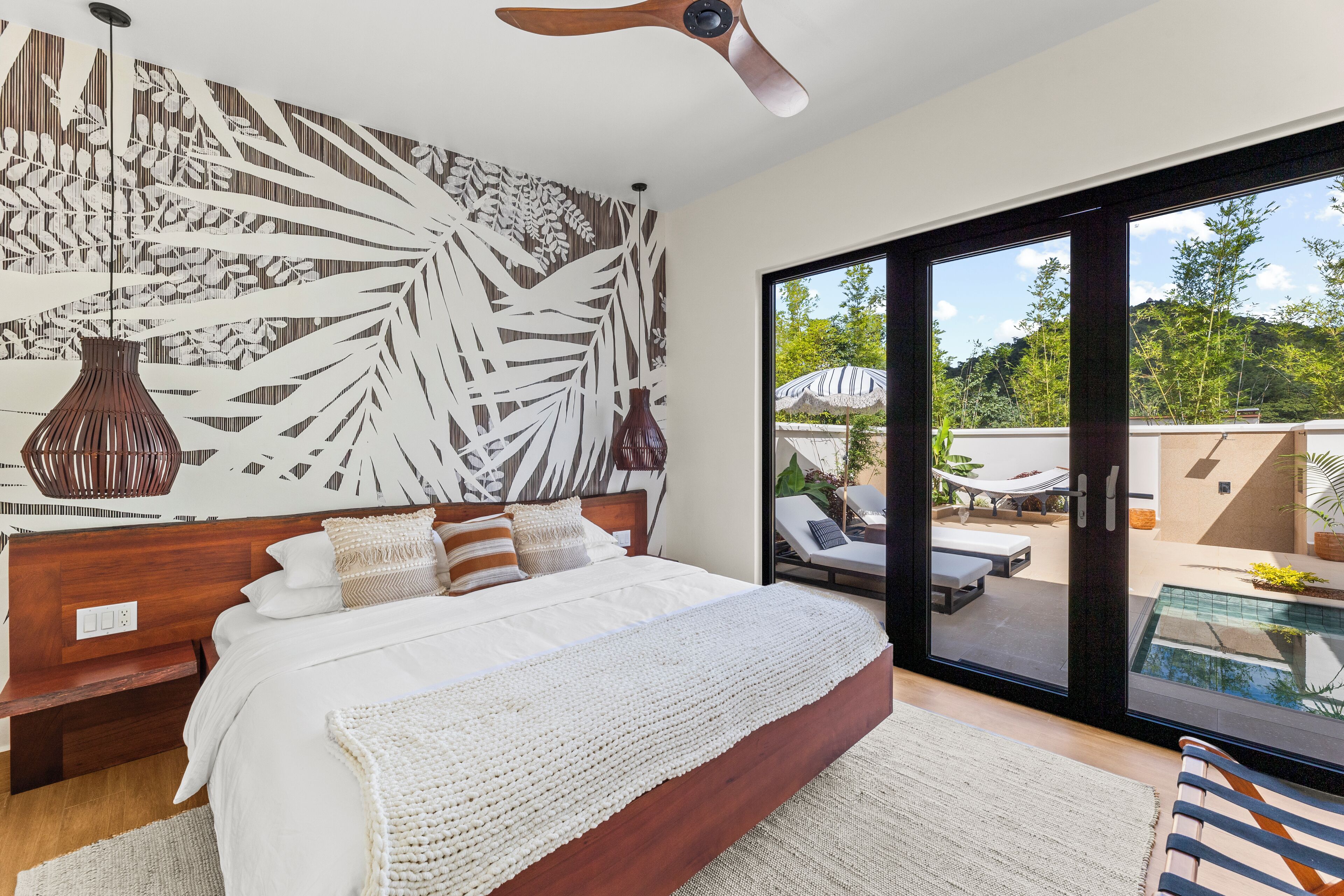 Ein Schlafzimmer mit einem großen Bett, einem Deckenventilator und Blick auf einen Außenpool.
