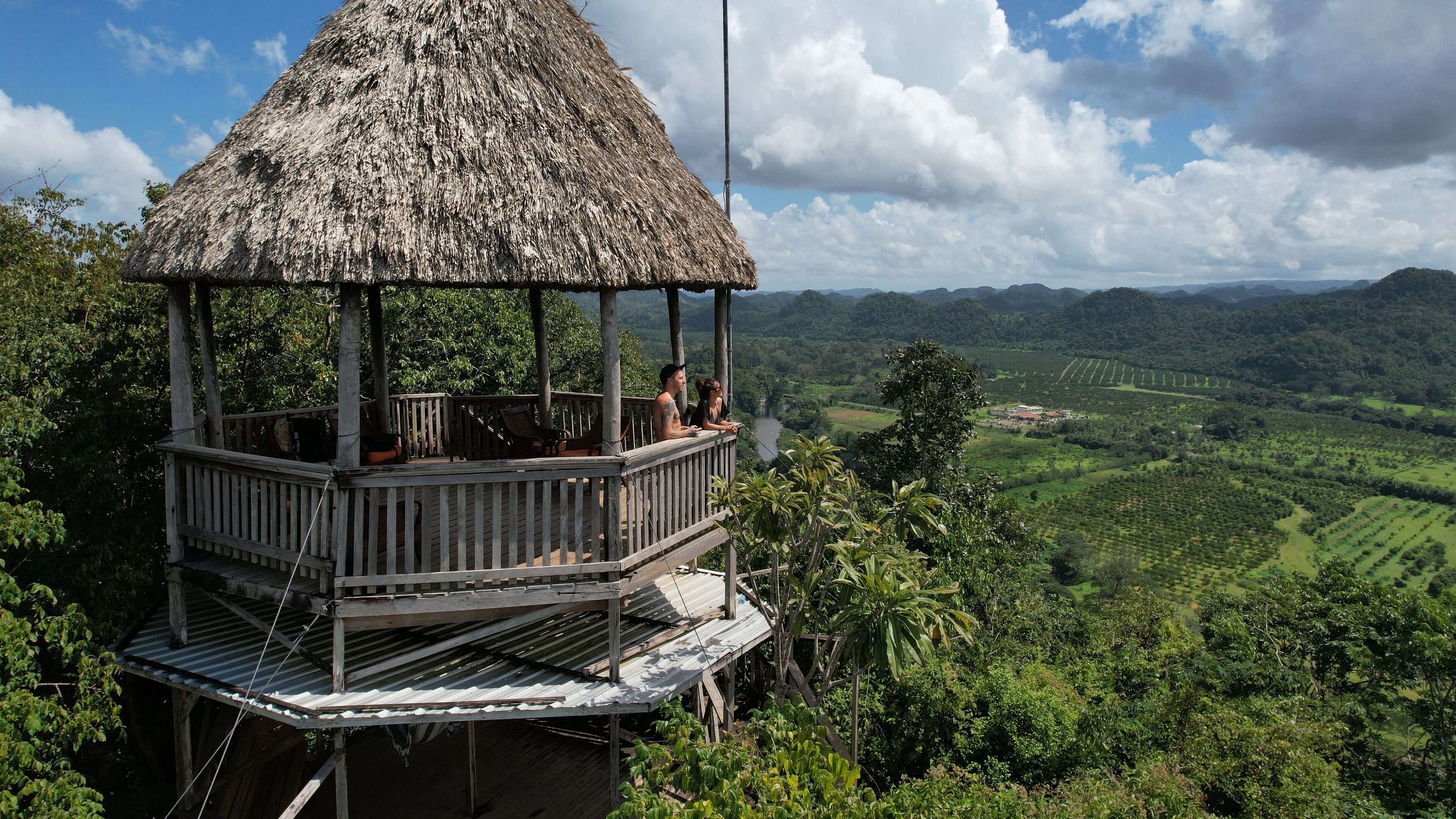 A wooden gazebo with a thatched roof overlooking a lush valley.