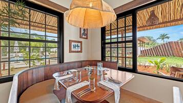 A dining area with a wooden table set for a meal, large windows with a view of the outdoors, and a hanging light fixture.