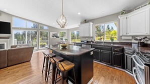 Una cocina amplia con una isla grande, muebles de color negro y blanco, y vistas al exterior.