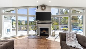Un salón amplio con chimenea, ventanas grandes y vistas a una terraza y piscina.