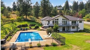 Una casa de dos pisos con piscina, rodeada por un patio cercado y abundante vegetación.