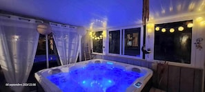 Ein Whirlpool mit blauer Beleuchtung, ein überdachter Bereich mit Fenstern und Lichterketten.