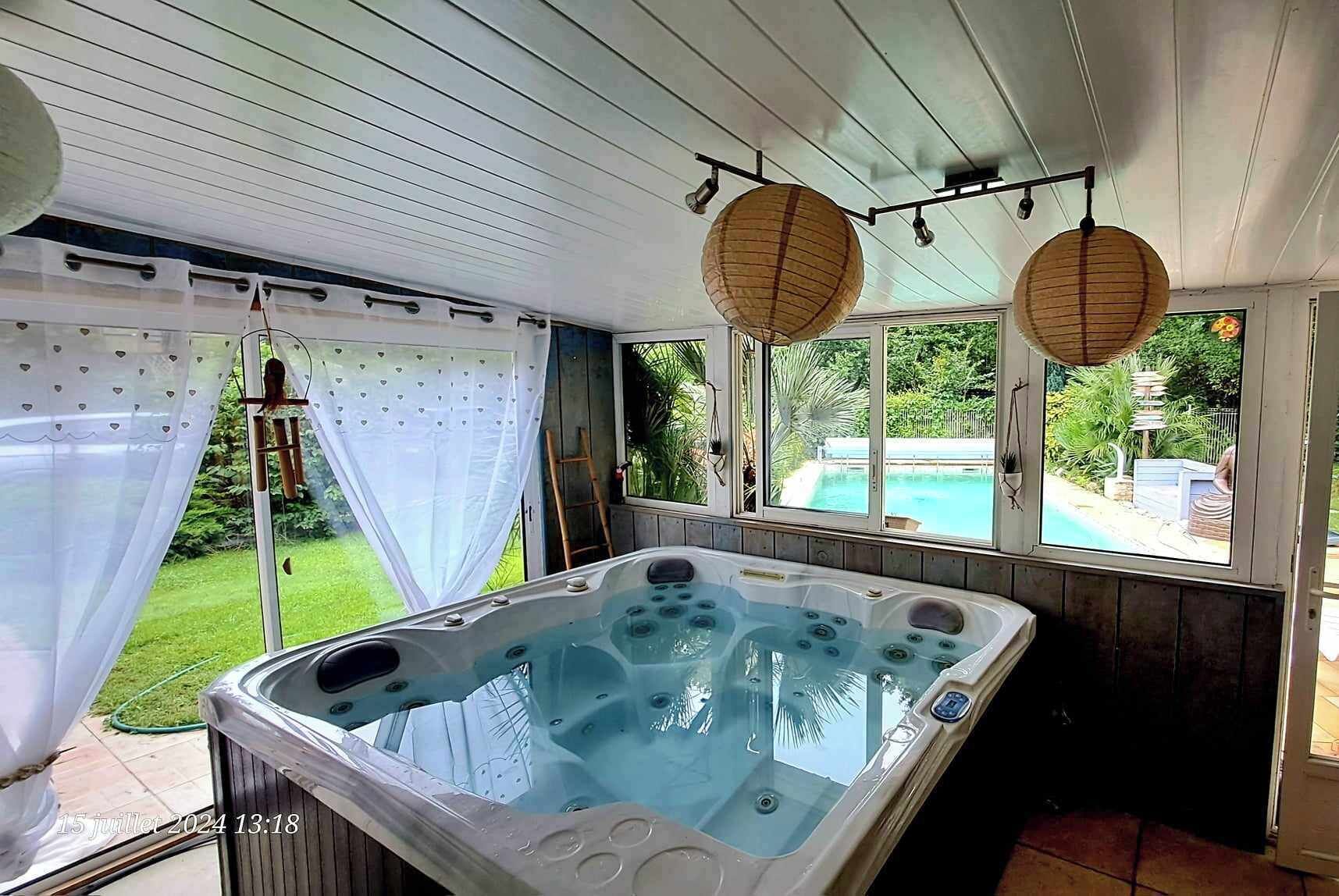 Ein Whirlpool in einer überdachten Außenbereich mit Blick auf ein Schwimmbad und Grünflächen.