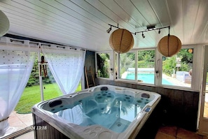 Ein Whirlpool in einer überdachten Außenbereich mit Blick auf ein Schwimmbad und Grünflächen.