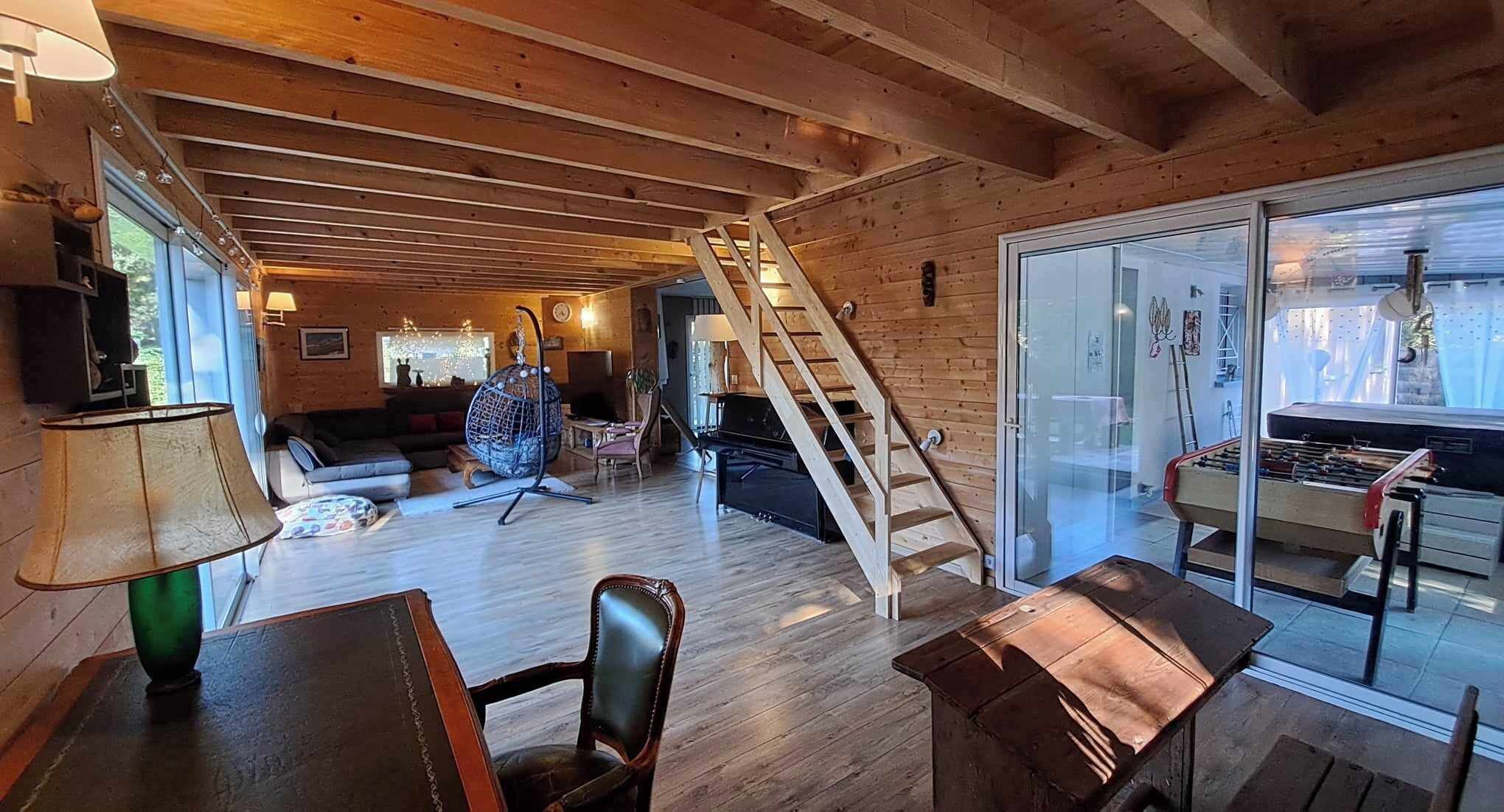 Ein gemütliches, holzgetäfeltes Interieur mit einer Treppe, die zu einer Glastür führt, einer Couch, einem Couchtisch und einem Kicker.