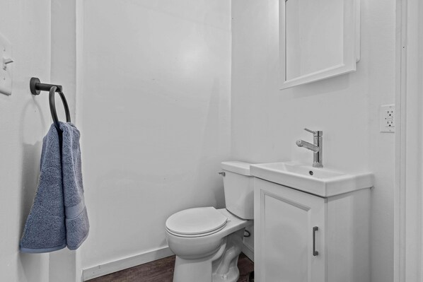 Un baño con un inodoro blanco, un lavabo y un perchero con dos toallas.