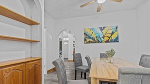 A dining area with a wooden table, grey upholstered chairs, a ceiling fan, and a large abstract painting on the wall.