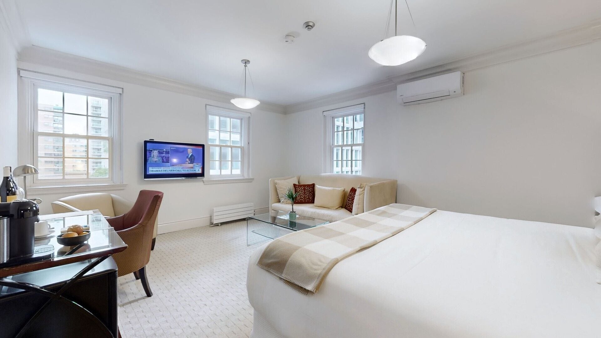 Una habitación de hotel con una cama grande, un escritorio con una silla, un televisor y dos ventanas.