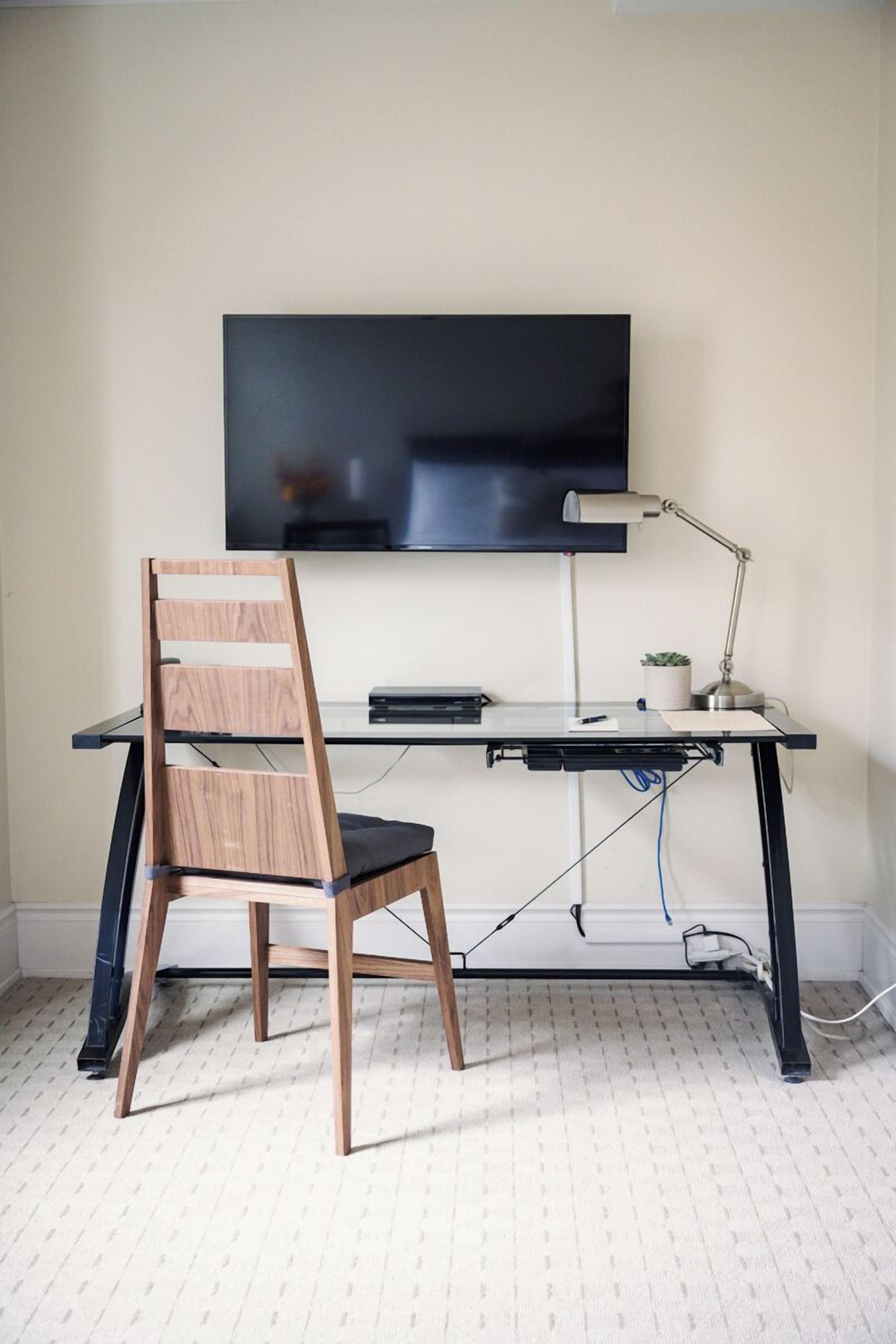 Ein moderner Arbeitsplatz mit Schreibtisch, Stuhl, Fernseher und Schreibtischlampe.