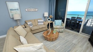 A living room with a beige sofa, a round coffee table, and a view of the ocean through a sliding door.
