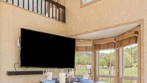 A dining area with a wooden table, two stools, a flat-screen TV mounted on the wall, and large windows offering a view of the outdoors. - Farm Stay Pool 15min to Chattanooga (Chattanooga)