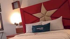 Une chambre d’hôtel avec un lit, une table de chevet, une lampe et un miroir fixé au mur.