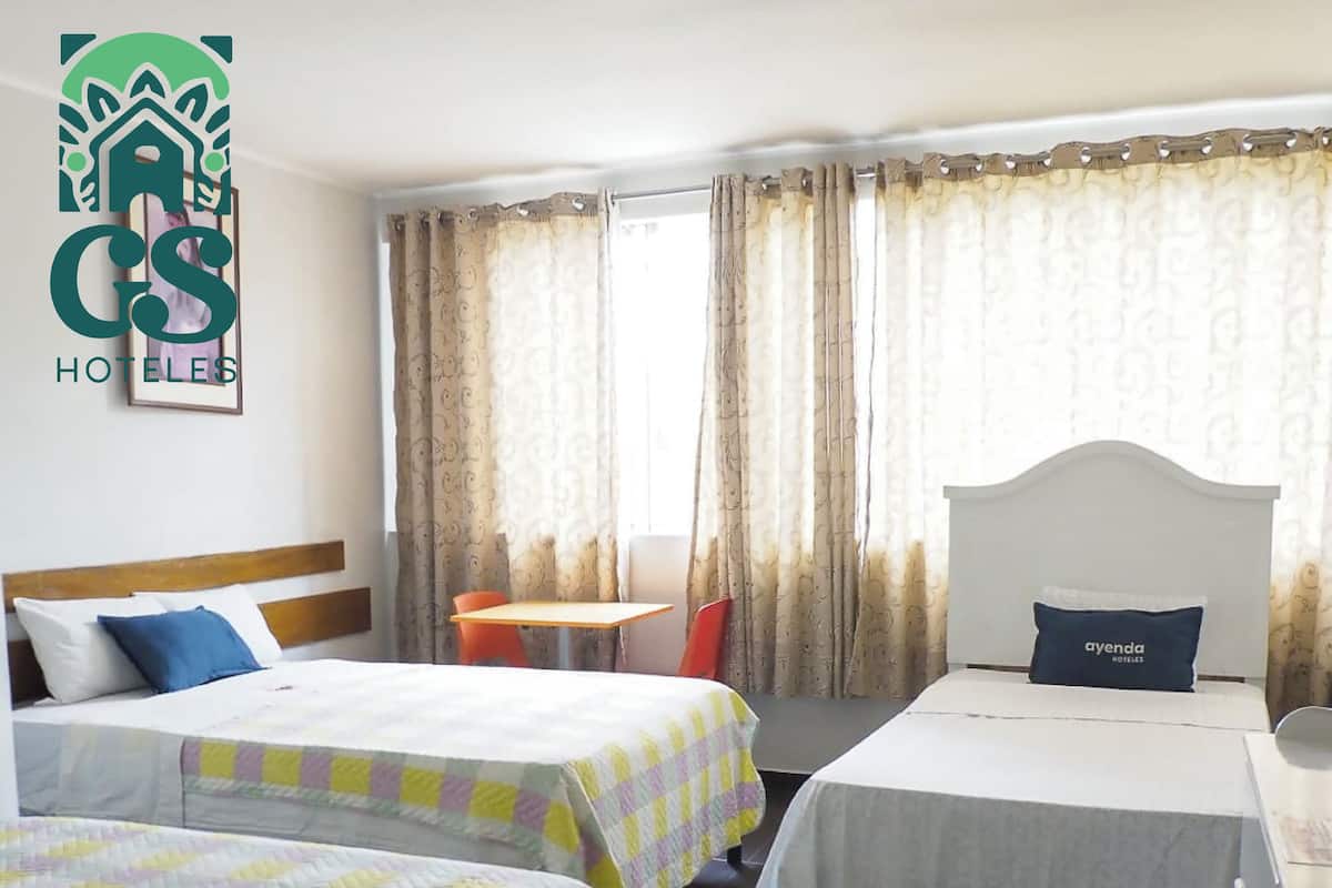 A hotel room with two beds, a small table, and a chair.