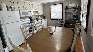 Een kleine keuken met witte kastjes, een magnetron, een fornuis en een eettafel met stoelen.