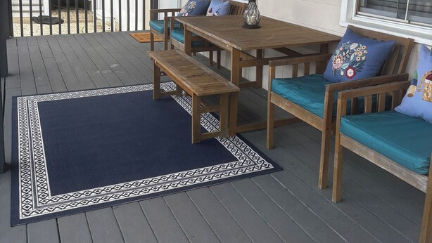 Een overdekt terras met houten meubels, een kamerkleed met dessin en een bord waarop 'hello' staat.