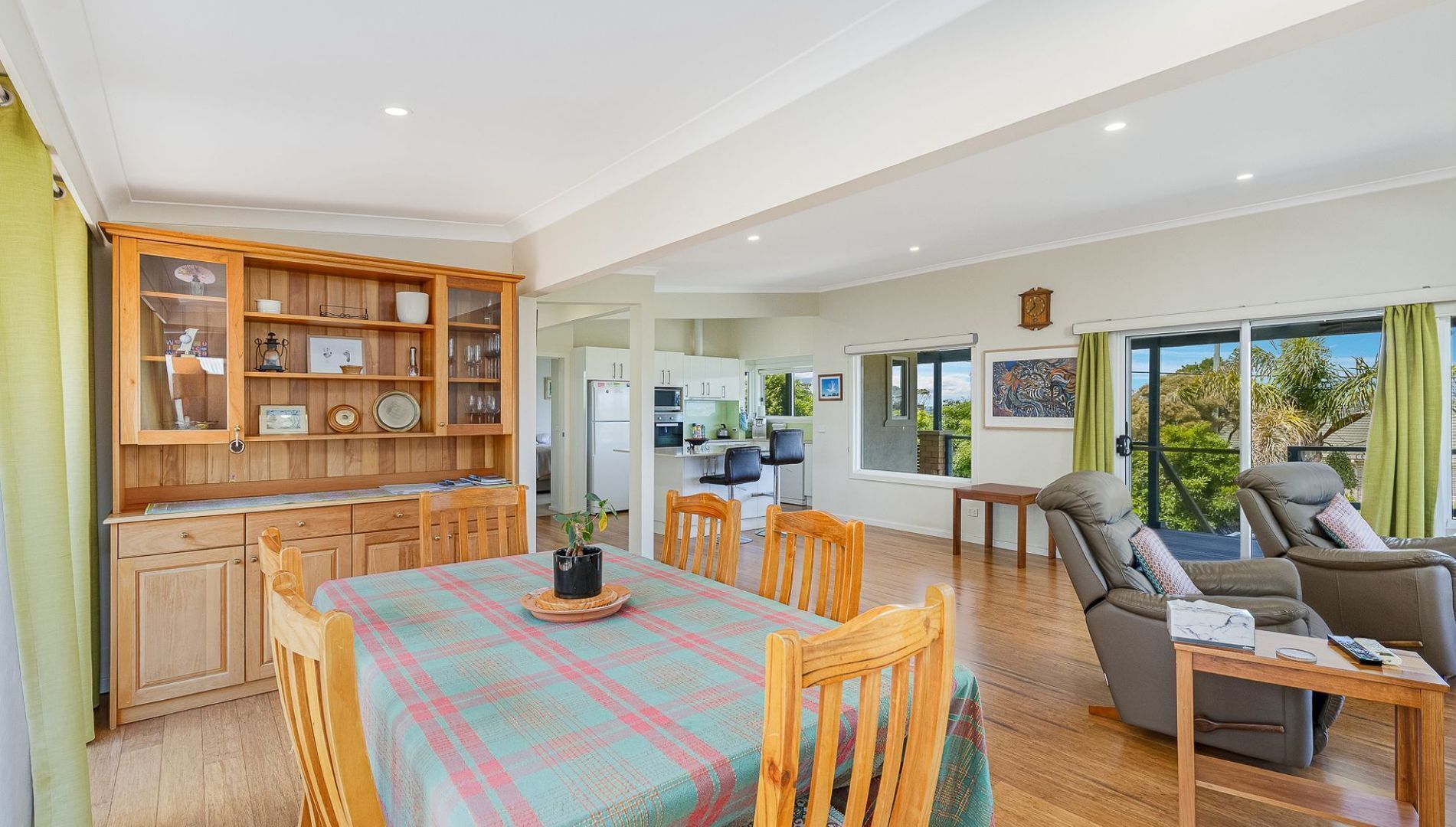 A spacious living area with a dining table, wooden chairs, a sofa, and a balcony with a view.