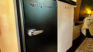 A compact, modern kitchenette with a black refrigerator labeled "Frigidaire," a small countertop, and a window above the sink.