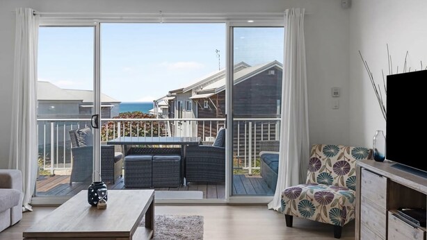 Een moderne woonkamer met een grote schuifpui die uitkomt op een terras met uitzicht op zee.