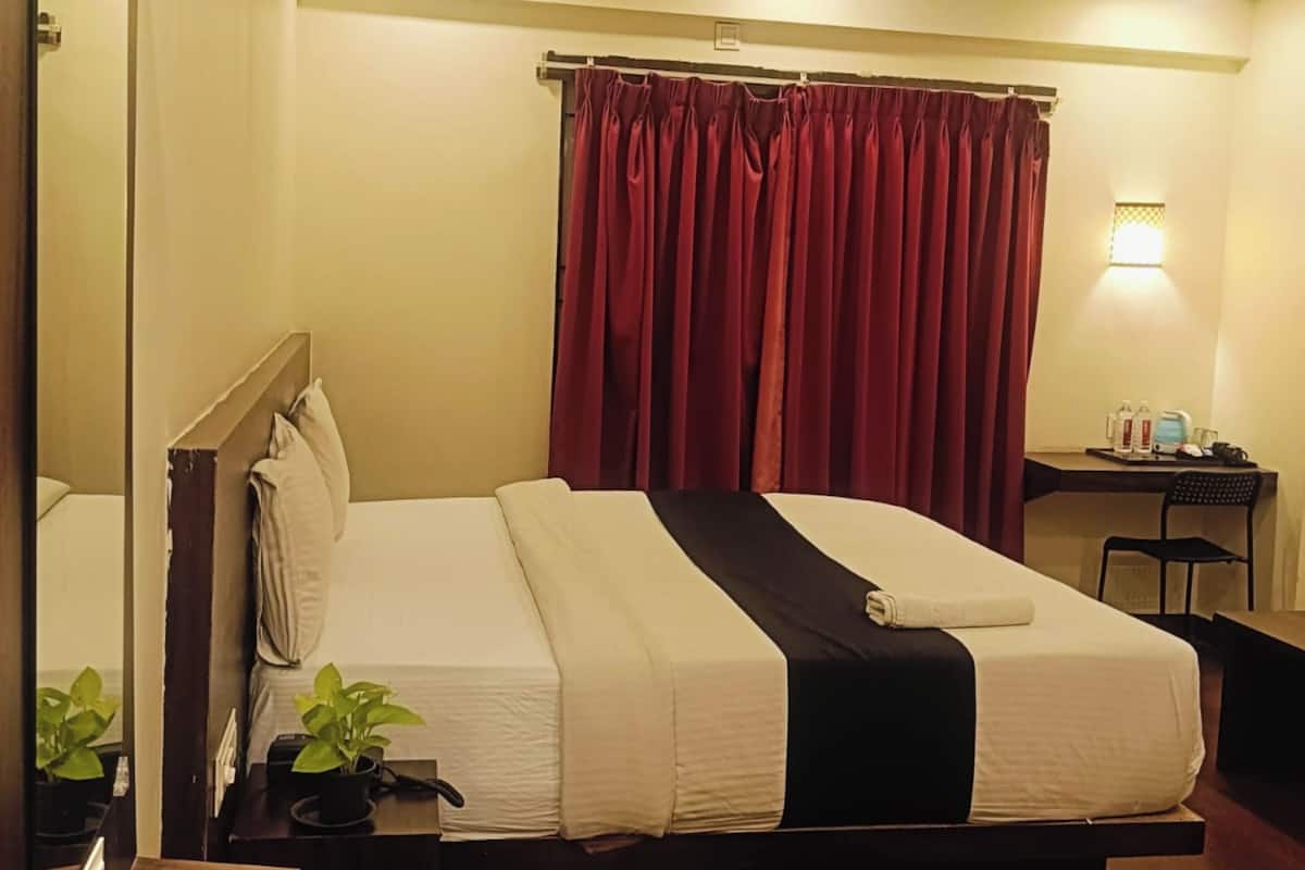 A hotel room with a large bed, a desk, a chair, a small table, a mirror, and a ceiling fan.