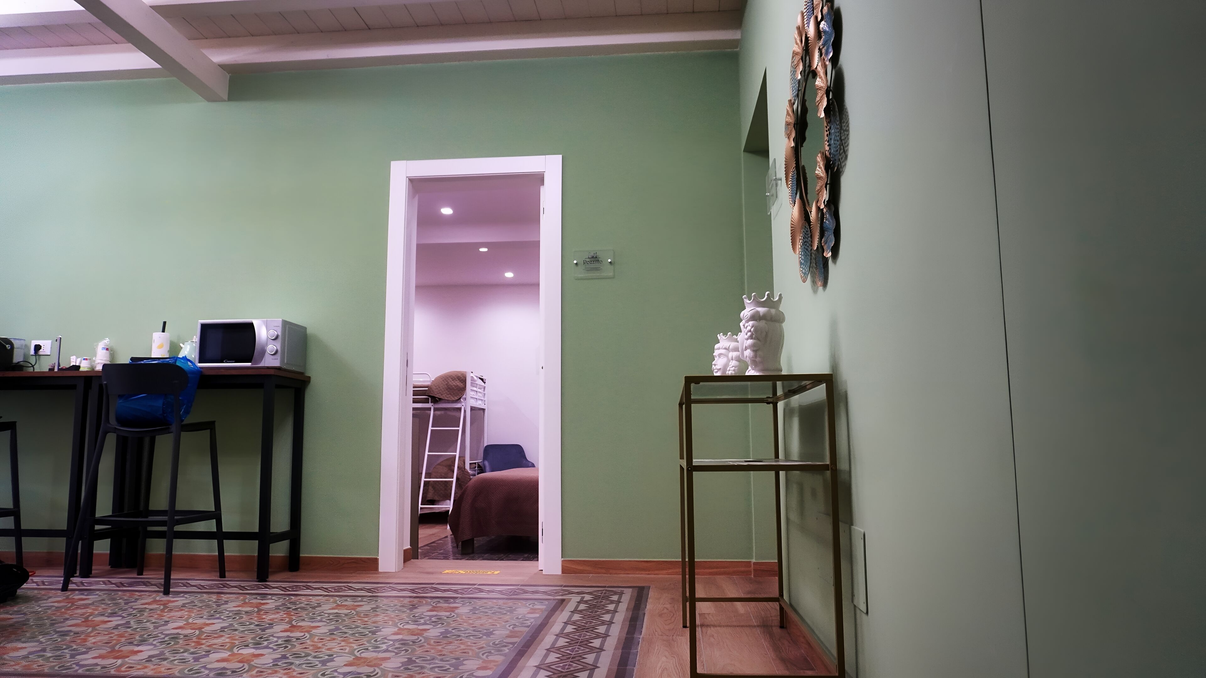 Une pièce comprenant un bureau, une chaise, une échelle, une petite table sur laquelle se trouve une statue, et un tapis à motifs.