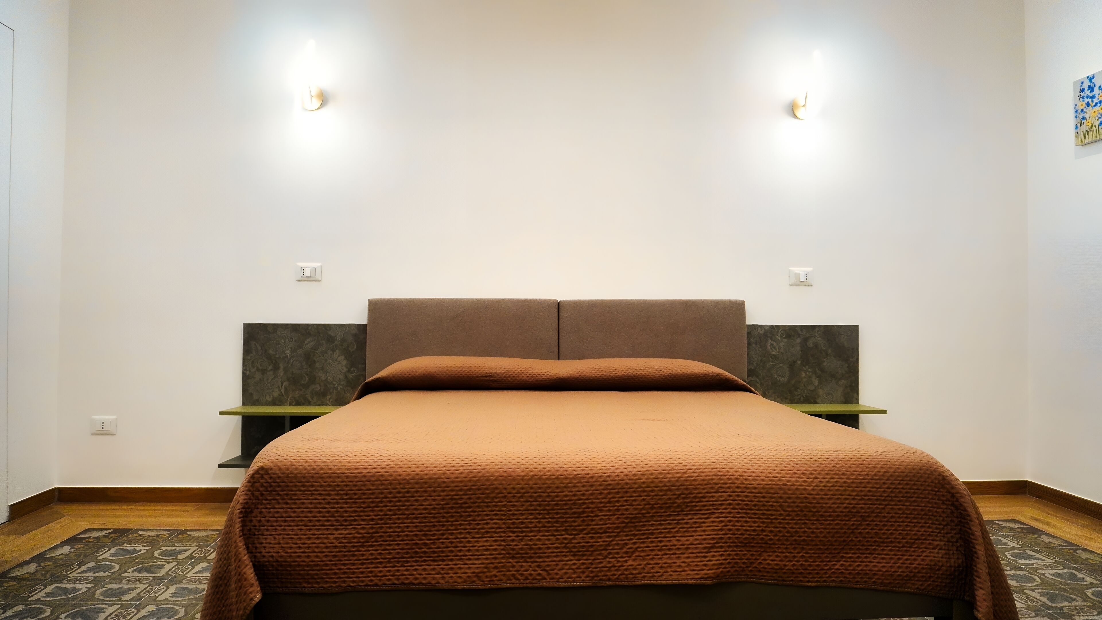 Une chambre à coucher bien rangée, avec une couverture de lit marron, deux tables de chevet et une tête de lit.