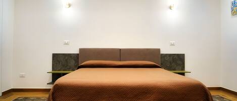 Une chambre à coucher bien rangée, avec une couverture de lit marron, deux tables de chevet et une tête de lit.