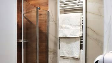 A modern bathroom with a glass shower enclosure, a white towel rack, and a hairdryer.
