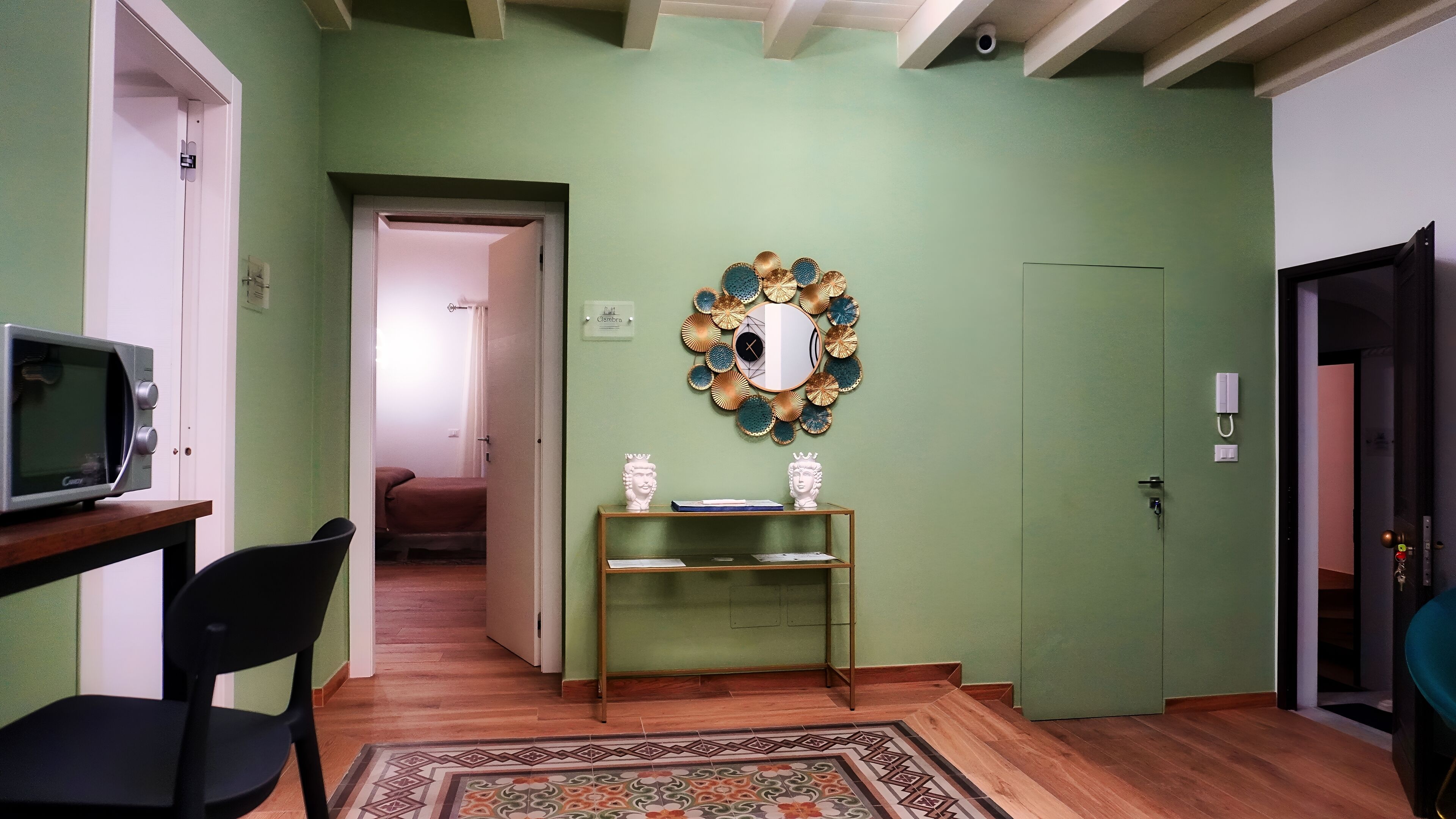 Un couloir avec un four à micro-ondes posé sur une table, une chaise, un miroir décoratif et une porte donnant sur une autre pièce.