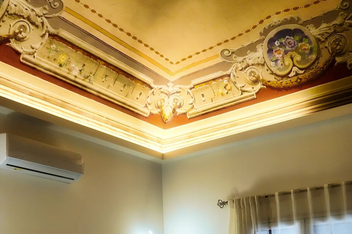 A hotel room with a large bed, an air conditioning unit, a wall-mounted light, and a window with curtains.