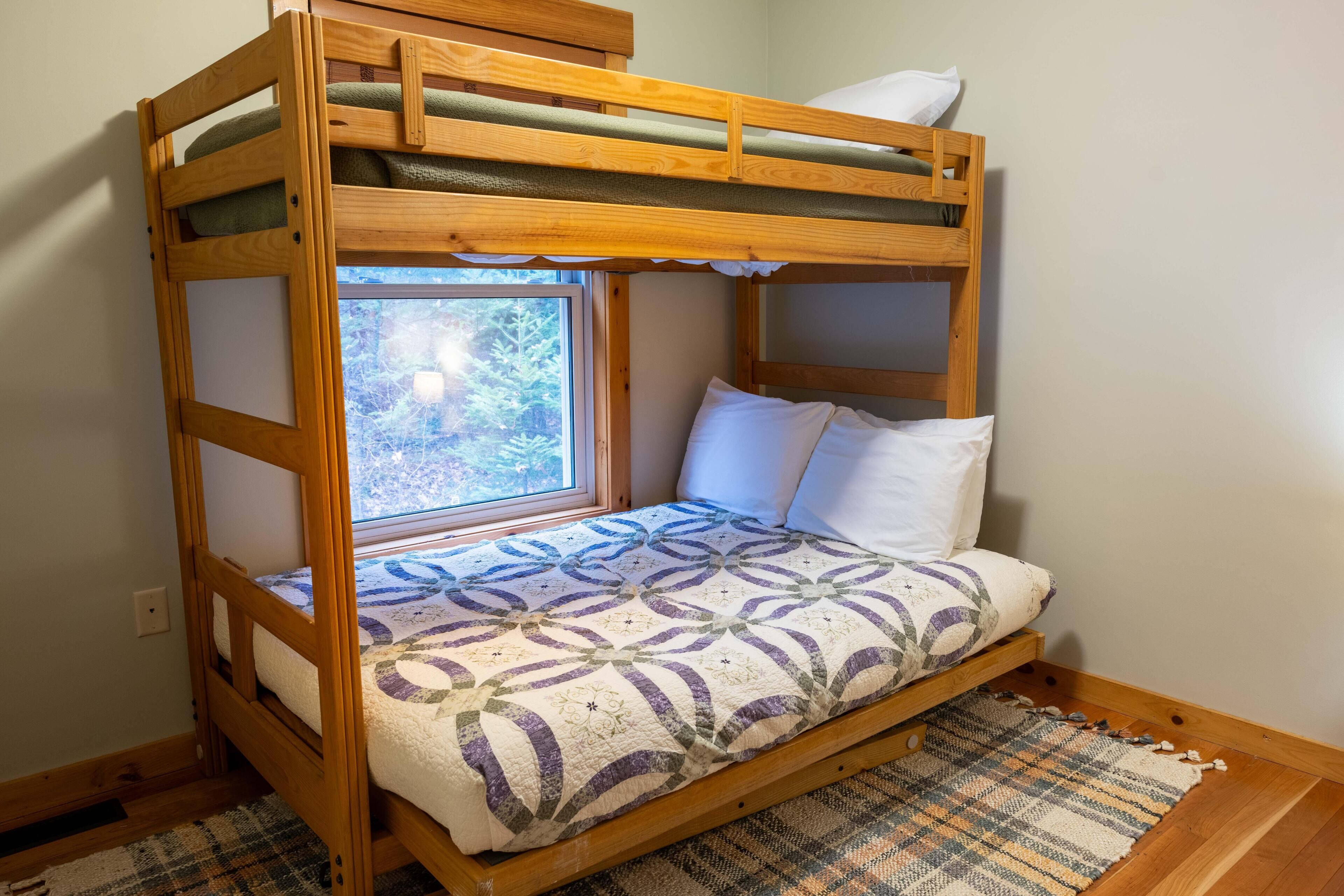 A bunk bed with a window, a patterned bedspread, and a woven rug on the floor.