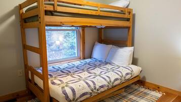 A bunk bed with a window, a patterned bedspread, and a woven rug on the floor.