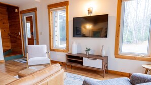 A living room with a leather sofa, a white armchair, a wooden entertainment unit, and a flat-screen TV mounted on the wall. - Sugarloaf Mountain Fir Avenue C3004 (Carrabassett Valley)