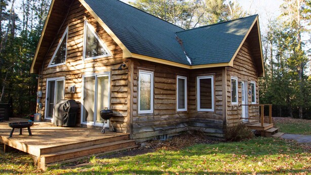 A log cabin with a steeply pitched roof, large windows, and a covered porch area. - Sugarloaf Mountain Fir Avenue C3004 (Carrabassett Valley)