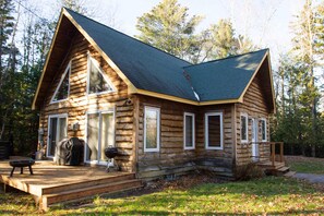 A log cabin with a steeply pitched roof, large windows, and a covered porch area.