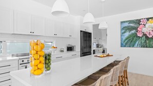 A modern kitchen with white cabinetry, a central island with fruit, and a dining area with wicker chairs.