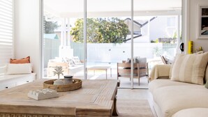 A modern living room with a wooden coffee table, a white sofa, and a view of a pool and outdoor furniture.