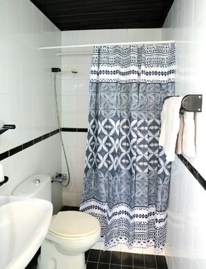 Bathroom features a white toilet, shower area with a geometric-patterned curtain, and a towel rack.