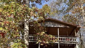 Een houten chalet met twee verdiepingen en een balkon, omgeven door bomen en herfstbladeren.